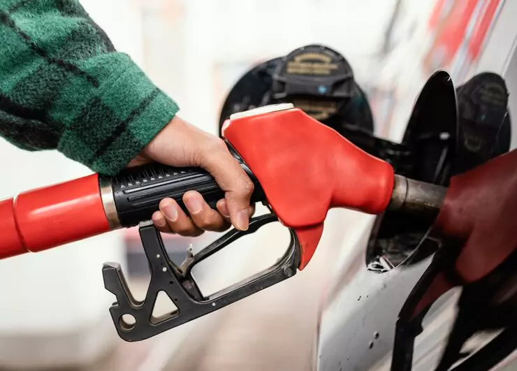 A person refueling a car with a red fuel pump nozzle at a gas station.