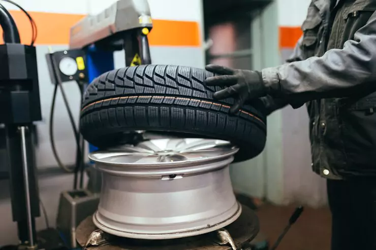 Mechanic fitting a new tyre onto an alloy wheel in a workshop.