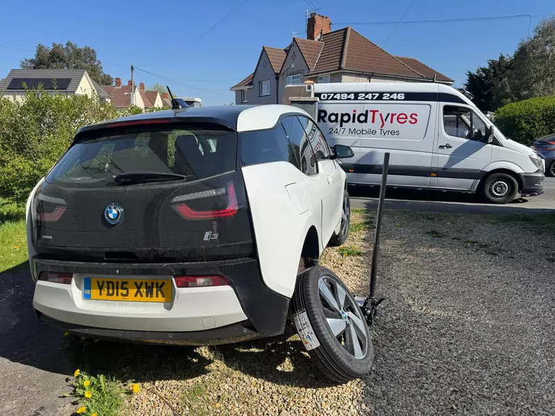 Mobile tyre fitting service in progress on a white BMW i3 by Rapid Tyres van in a residential area.