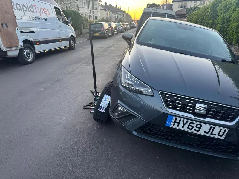 Rapid Tyres mobile technician fitting a new tyre on a grey SEAT car parked on a residential street.