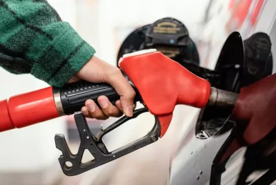 A person refueling a car with a red fuel pump nozzle at a gas station.